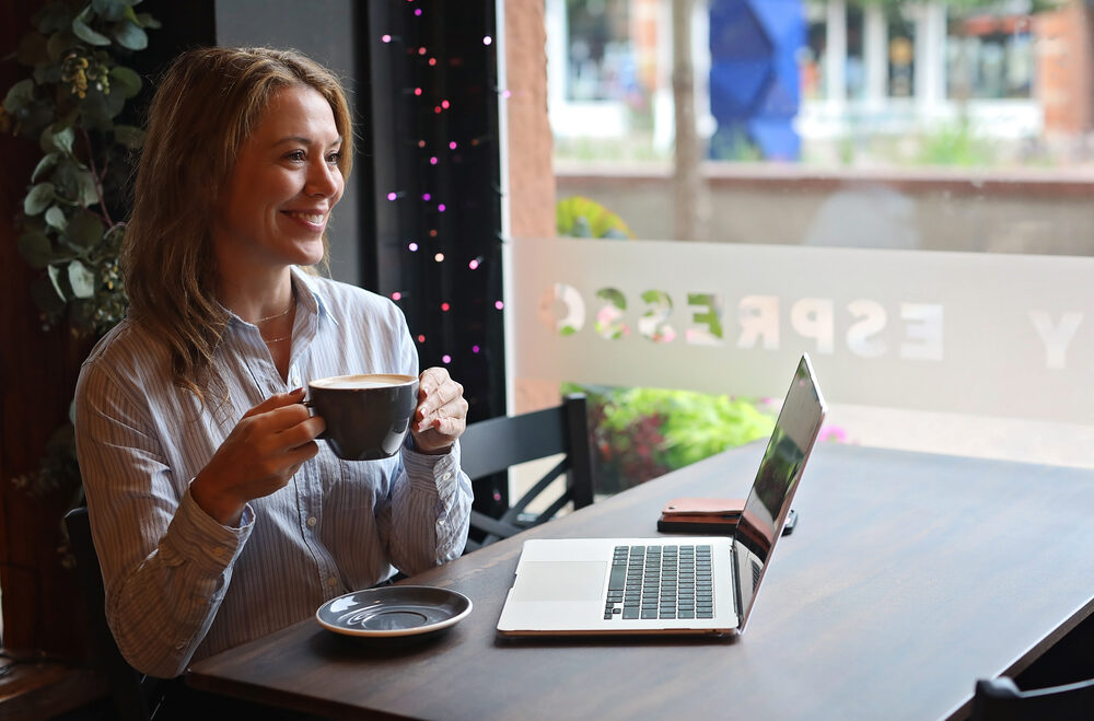 Faye Bonomo smiling over a cup of coffee at a café table with a laptop open beside her