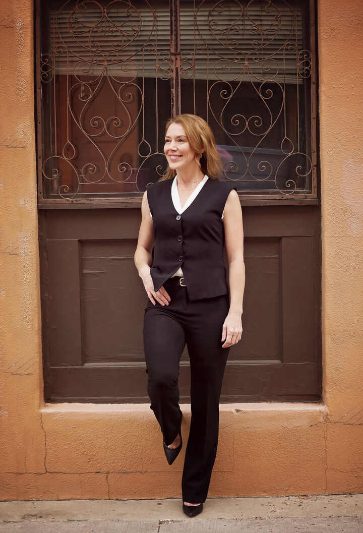 Faye Bonomo in a black vest standing in front of an ornate iron-grilled doorway